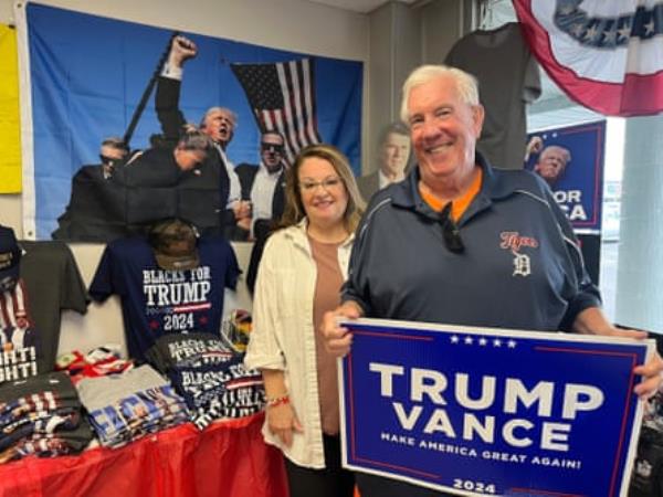 a woman and man smile at camera as man holds a blue poster